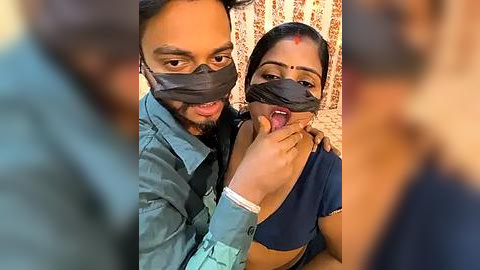 Media: Video of a couple wearing gray duct tape over their mouths, with the woman touching her partner's tongue with her fingers, in a domestic setting with floral curtains.