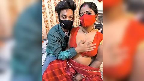 Media: A video shows two South Asian women, one with medium skin, wearing a red saree and red face mask, and another with fair skin, a black face mask, and a green jacket, hugging each other in a domestic setting with floral curtains.