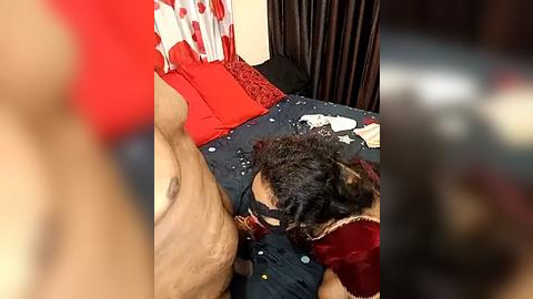 Media: Video of a man lying face-down on a bed, a black dog lying on his back. The bed has red and white bedding, with scattered clothes. The room has a dark, cluttered feel.