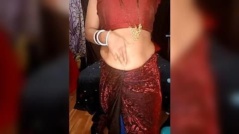 Media: A video of a woman with a medium skin tone, wearing a red, intricately patterned sari and a matching blouse, standing in a room with wooden floors.