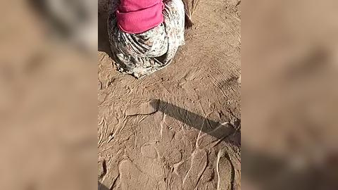 Media: Video of a person's lower leg and foot in a sandy environment, wearing a pink sock and white sandal, with a blurred background.