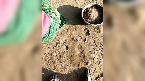 Media: Video of a sandy beach with a green and pink sand bucket, a white pail, and a metal shovel. The image captures a playful outdoor scene.