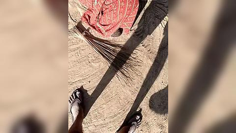 Media: A video capturing a man wearing black flip-flops and shorts, walking on a sandy surface, with a red and white woven mat in the background.