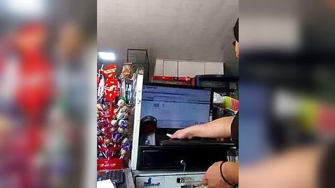 Media: Video of a person in a supermarket aisle, wearing a black shirt, using a touchscreen to scan items; shelves filled with snacks, boxes, and products in the background.