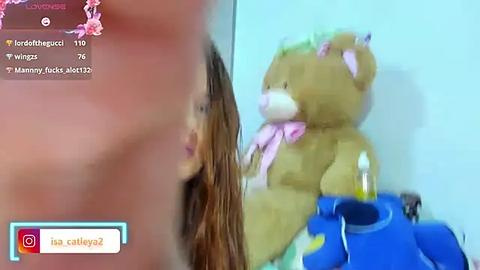 Media: Video of a blurred, partially naked person with long brown hair and a large, pink ribbon on a teddy bear in a blue room, with social media icons at the top.