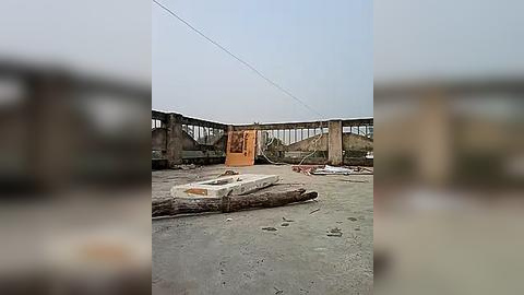 Media: Video of a dilapidated construction site with a wooden scaffold and partially built structure, set against a cloudy sky. The ground is littered with debris, and the overall scene conveys abandonment and neglect.