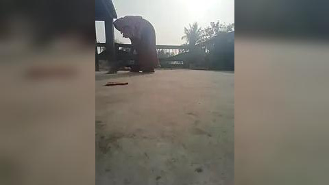 Media: A blurry video shows a person in a dark robe kneeling on a concrete floor, possibly praying, with a metal object on the ground. The background features an outdoor setting with trees and structures.