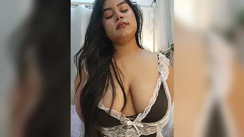 Media: Video of a Latina woman with long black hair, wearing a revealing black lace lingerie top with white trim, eyes closed, in a softly lit bathroom.