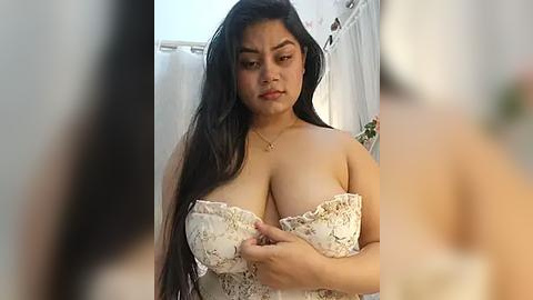 Media: A video of a plus-sized woman with long black hair and medium skin tone, wearing a strapless white lace dress, adjusting the dress straps in a bathroom. The background features a white shower curtain and floral decor.