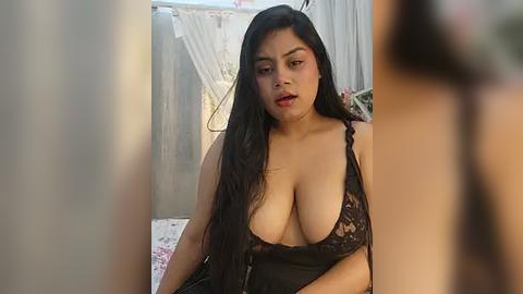 Media: A video of a South Asian woman with long black hair, wearing a revealing black lace lingerie top, sitting indoors against a backdrop of laundry and fabric.