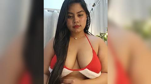 Media: Video of a Latina woman with long black hair, wearing a red bikini top with white trim, standing in a garden with blurred background.