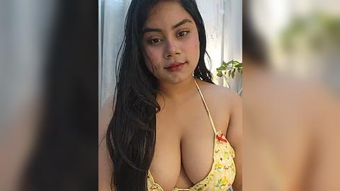 Media: Video of a young, curvy Latina woman with long black hair and medium skin tone, wearing a low-cut floral bikini top, indoors with blurred background.