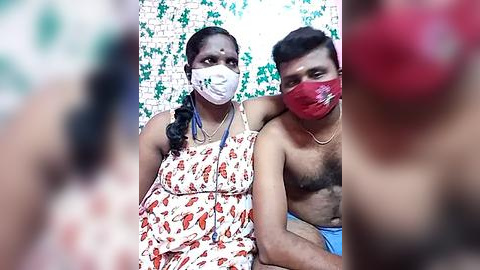 Media: Video of an Indian couple wearing masks, with the woman in a floral dress and the man shirtless, in a tiled room with green plants.