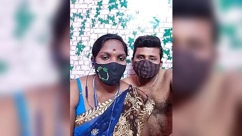 Media: Video of two Indian women wearing face masks and traditional sarees, against a white brick wall adorned with green vines. One has a blue saree, the other a gold-patterned one.