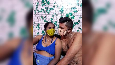 Media: Video of a Black man with short hair and a Black woman with braided hair, both masked and shirtless, sitting on a white brick wall with green ivy.