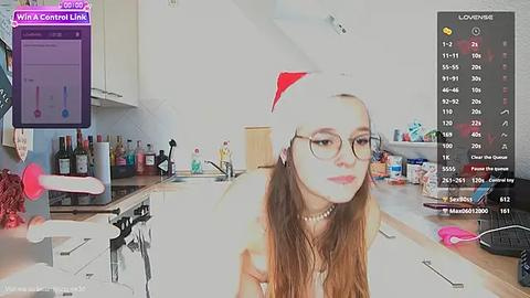 Media: Video of a young woman with glasses, wearing a red Santa hat and a white dress, in a modern kitchen, with a live stream overlay of chat messages.