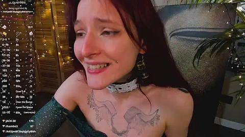 Media: Video of a smiling woman with fair skin, red hair, and multiple facial piercings, wearing a glittery off-shoulder dress, adorned with a choker and tattoos.