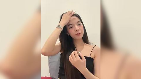 Media: Video of an Asian woman with long black hair, wearing a black spaghetti strap dress, touching her hair, against a plain white background.