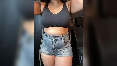 Media: Video of a woman in a black sports bra and high-waisted denim shorts, standing in a car with the door open.