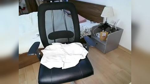 Media: A video of a messy bedroom with a black office chair, white blanket, and cluttered nightstand, featuring a lamp, cup, and a folded blanket.