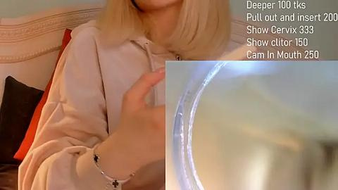 Media: Video of a blonde woman in a white robe, sitting on a bed with a headboard, revealing a glimpse of a transparent, cylindrical object. Text overlay indicates \"Deep Throat\" and \"Pull out and insert\" instructions.