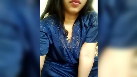 Media: Video of an Asian woman with long black hair, wearing a deep blue satin dress with intricate lace detailing and a plunging neckline. Her face is partially visible, with full lips and a slight smile.