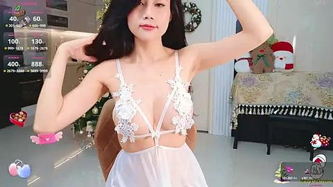 Media: Video of an East Asian woman in a sheer white lingerie bodysuit with floral lace, posing indoors by a Christmas tree and festive decor.