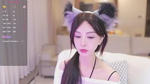 Media: A video of an East Asian woman with long, dark hair, wearing grey wolf ears and a black top, sitting in a modern, minimalist living room.