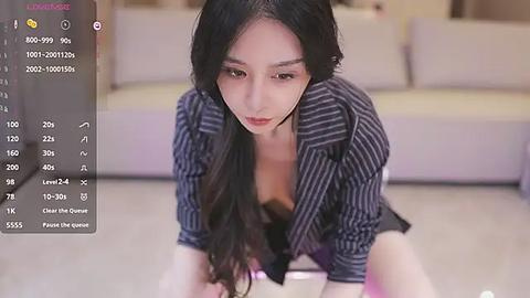 Media: A video of an East Asian woman with long black hair, wearing a striped shirt, kneeling on a light-colored floor in a living room. The background shows a beige couch and soft lighting.