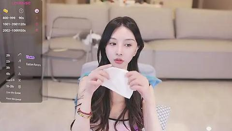 Media: Video of an Asian woman with long black hair, holding a tissue, in a modern living room with beige couches and a glass table.