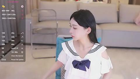 Media: A video of an Asian woman with straight black hair, wearing a white sailor-style top with a blue bow, sitting on a beige sofa in a modern living room.