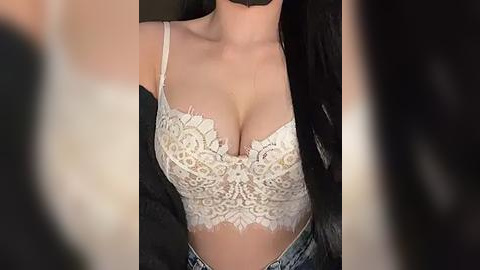 Media: Video of a woman's upper torso in a white lace bra, showcasing her ample cleavage and fair skin. She wears a black jacket, and her long black hair flows over her shoulders. The background is blurred.