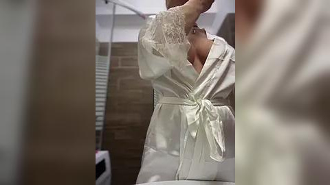 Media: A video of a person in a white satin robe with lace trim, adjusting a towel in a bathroom with tiled walls and a white door.