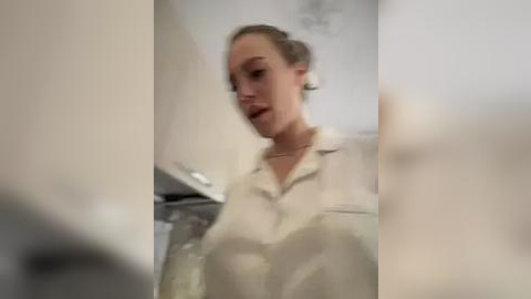 Media: A video of a young woman with light skin, short blonde hair, and a white blouse, captured in a blurred bathroom scene.