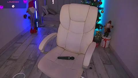 Media: Video of a modern, white leather office chair with a black microphone on the seat, set in a dimly lit room with a decorated Christmas tree and colorful lights, featuring a Santa Claus doll and a wrapped gift box.