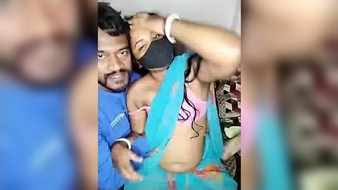 Media: Video of a South Asian man in a blue shirt holding a young child in a pink top, both wearing face masks, in a blurry, dimly lit room.