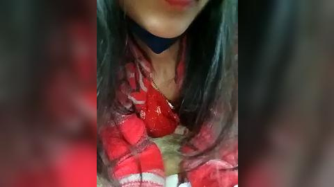 Media: A close-up video of a person wearing a red, fuzzy sweater with a blue choker and a gold necklace, featuring long black hair. The image is slightly blurred, emphasizing the textures and colors.