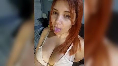 Media: A video of a young woman with light skin and straight red hair, wearing a white bra, sticking out her tongue playfully.