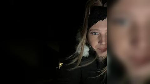 Media: A video of a blonde woman with a black headband and fur-trimmed jacket, peering through a dark, blurry window, revealing a dimly lit, indistinct outdoor scene.