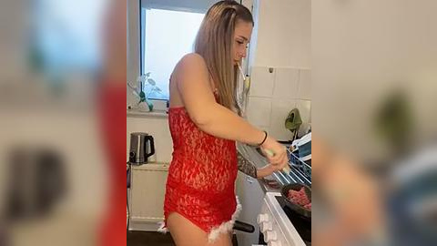 Media: Video of a woman in a red lace lingerie outfit, cooking in a kitchen with a white stove, beige walls, and a window.