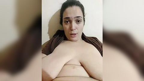 Media: Video of a light-skinned woman with dark hair, partially exposed breasts, wearing a brown shirt, taken from a slightly blurred, close-up perspective.