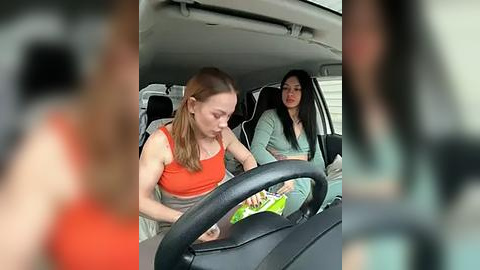 Media: Video of two young women, one with red hair and orange top, the other with black hair and green top, driving in a car.