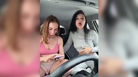 Media: Video of two women in a car; one in pink lingerie, the other in a grey sweater. They are engrossed in their phones, with blurred figures in the background.