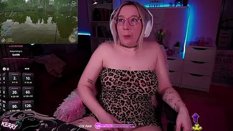 Media: Video of a plus-sized woman with glasses, leopard-print dress, and headphones, seated in a cozy, dimly-lit room with video game screens and furniture.