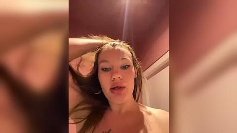 Media: Video of a young woman with light skin, wet hair, and a confused expression, taken from a slightly blurred angle, indoors with warm lighting.