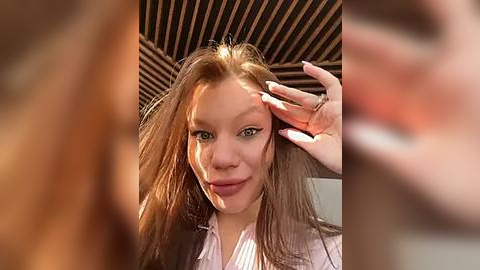 Media: A video of a young woman with long brown hair, fair skin, and blue eyes, wearing a white shirt, standing under a wooden ceiling.