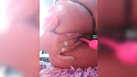 Media: Video of a close-up, blurred face with closed eyes and a pink vibrator inserted into the mouth. Background shows a purple, textured blanket.