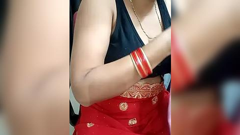 Media: Video of a woman wearing a red saree with gold embroidery and a black sleeveless blouse, adorned with red bangles.