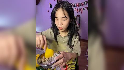 Media: Video of a young Asian girl with long black hair, wearing a beige T-shirt, stirring a yellow liquid in a bowl, surrounded by festive decorations.