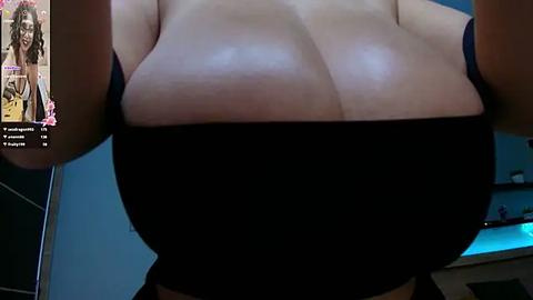 Media: Video of a woman with light skin, large breasts, wearing a black strapless top, taken from a selfie perspective. Background includes a blue wall and a framed picture of a woman in a yellow dress.